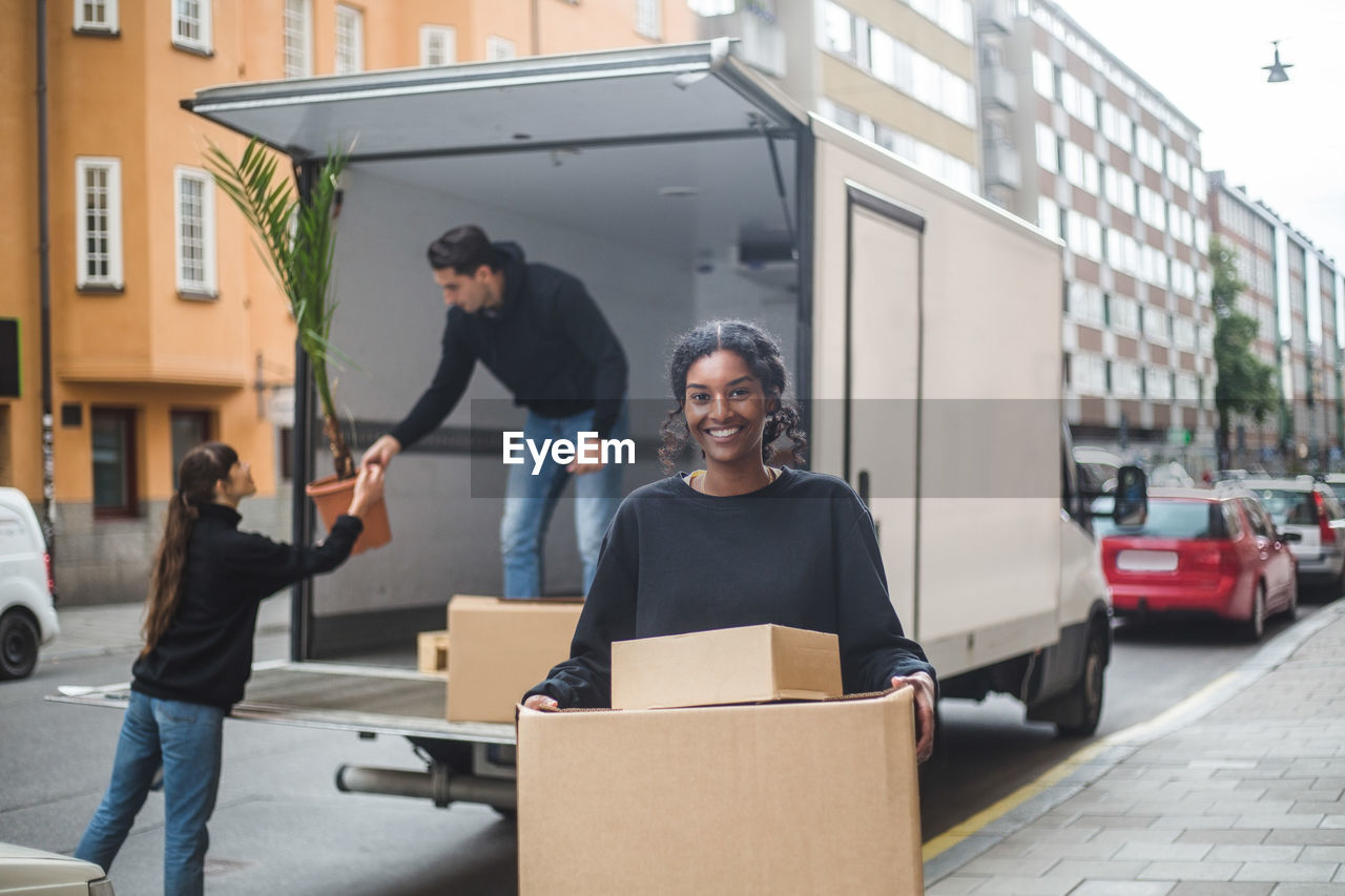 Portrait of confident female mover carrying cardboard boxes