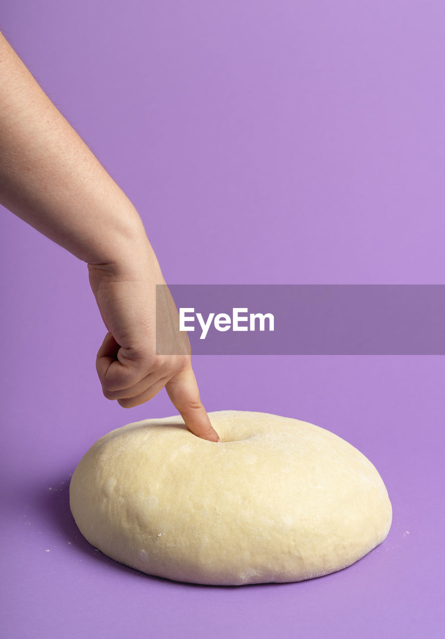 Leavened bread dough isolated on a purple background. woman checking dough. home baking bread buns.