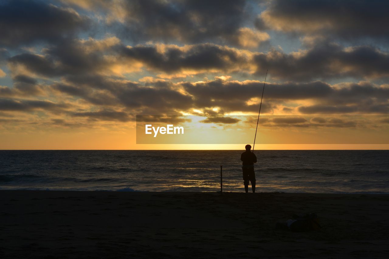 SILHOUETTE MAN FISHING ON BEACH AT SUNSET