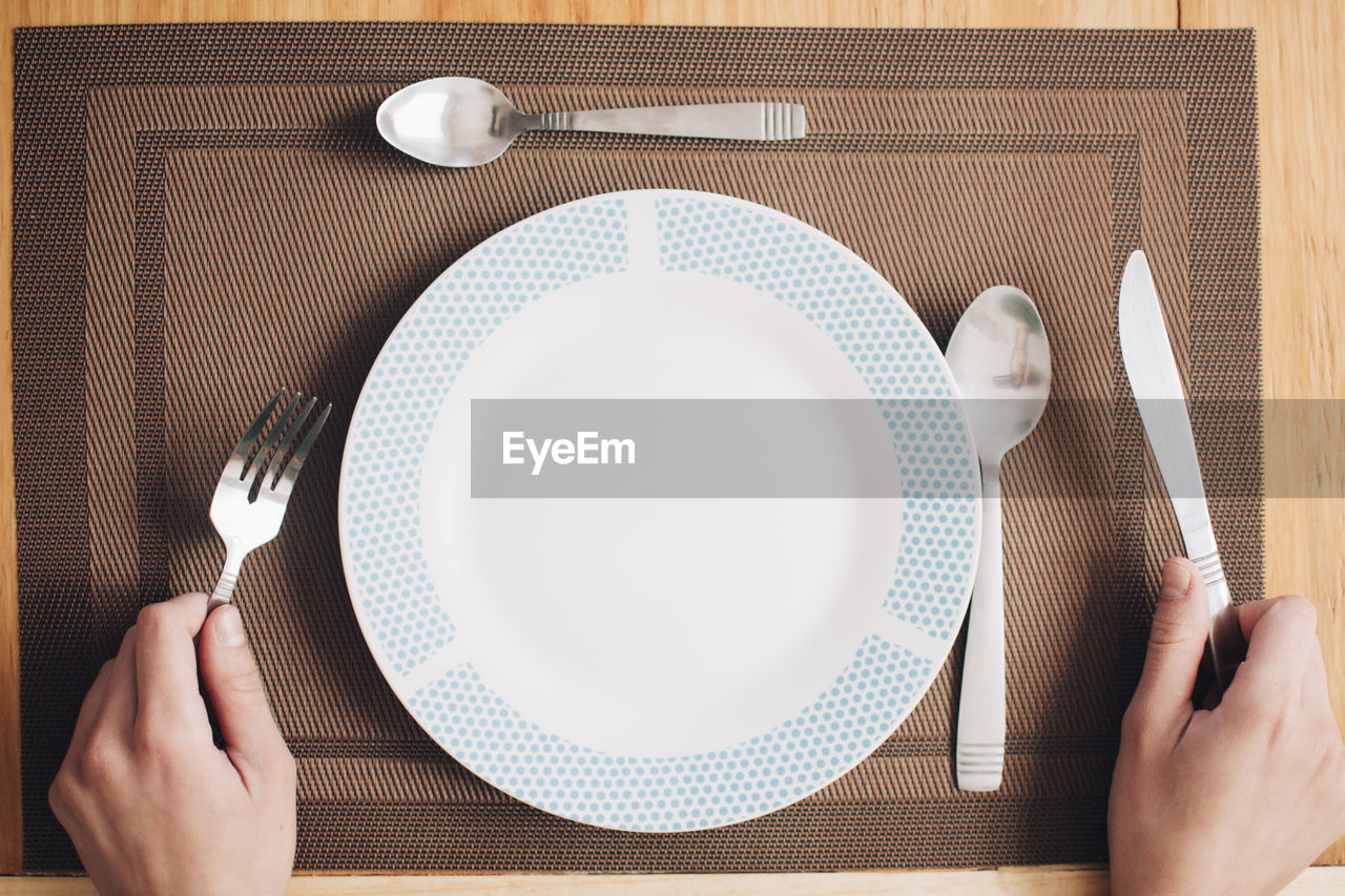 Cropped hands of man holding eating utensil on table