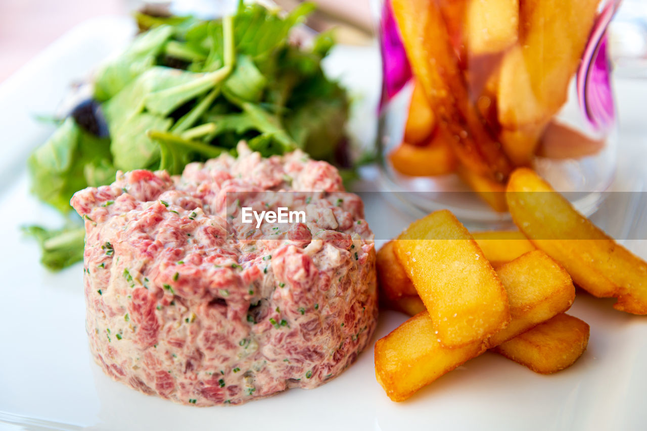 Close-up of beef tartare on plate served with french fries and fresh lettuce on white plate