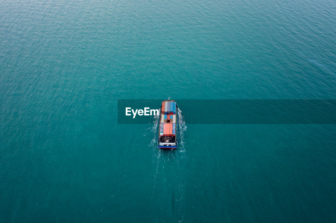 Aerial top view container ship sailing on the green sea full speed container for logistics, import 