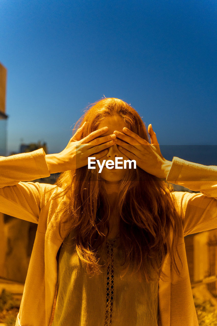 Young woman with hand on her eyes at blue hour