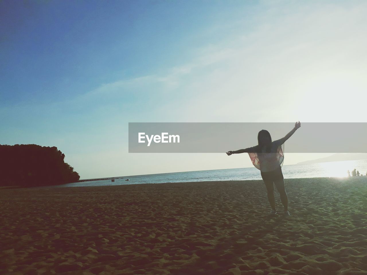 Woman with arms outstretched standing on sand at beach against sky