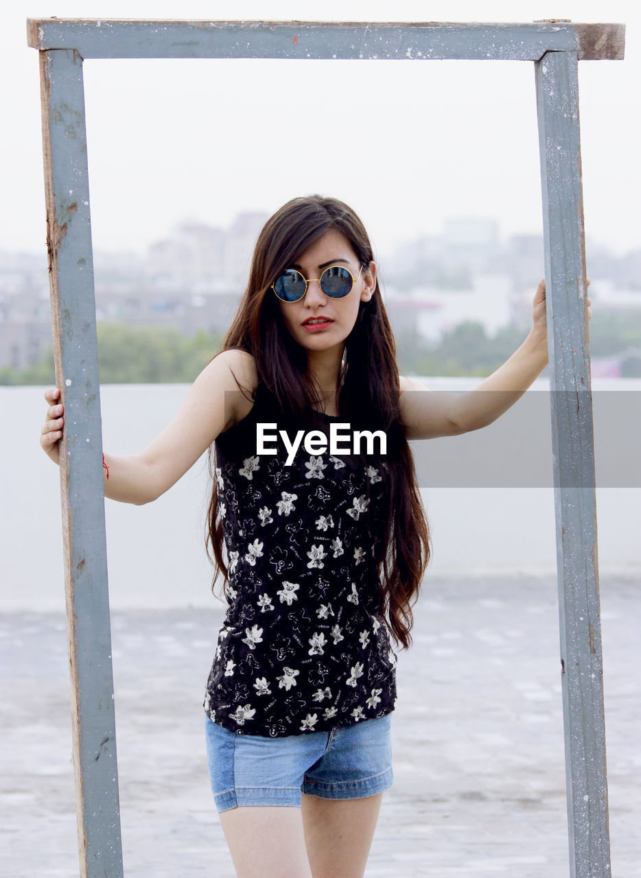 Beautiful woman holding wooden frame against river