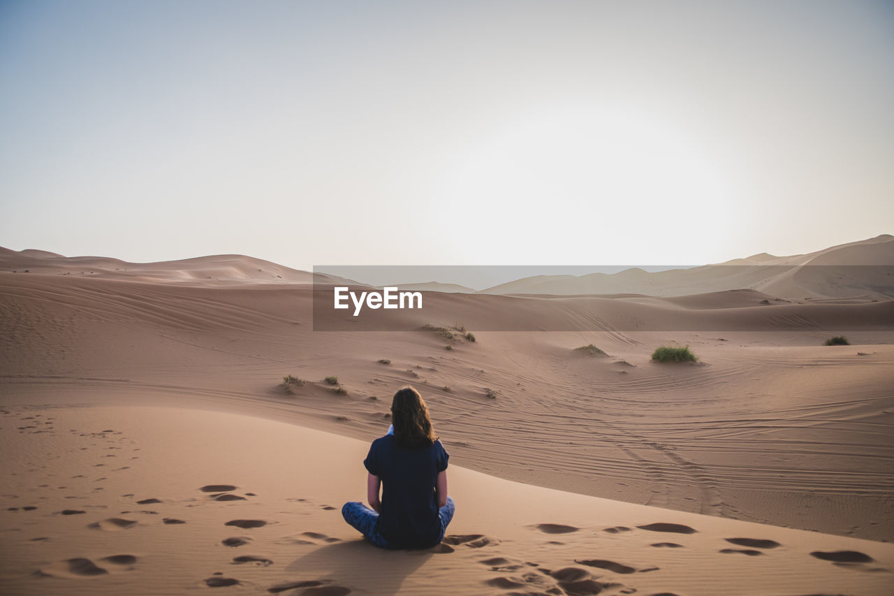 Rear view of woman sitting on desert against sky