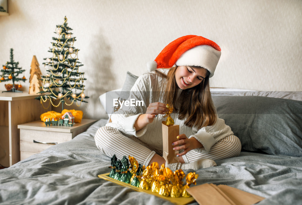 Smiling teenage girl making christmas gift while sitting on bed