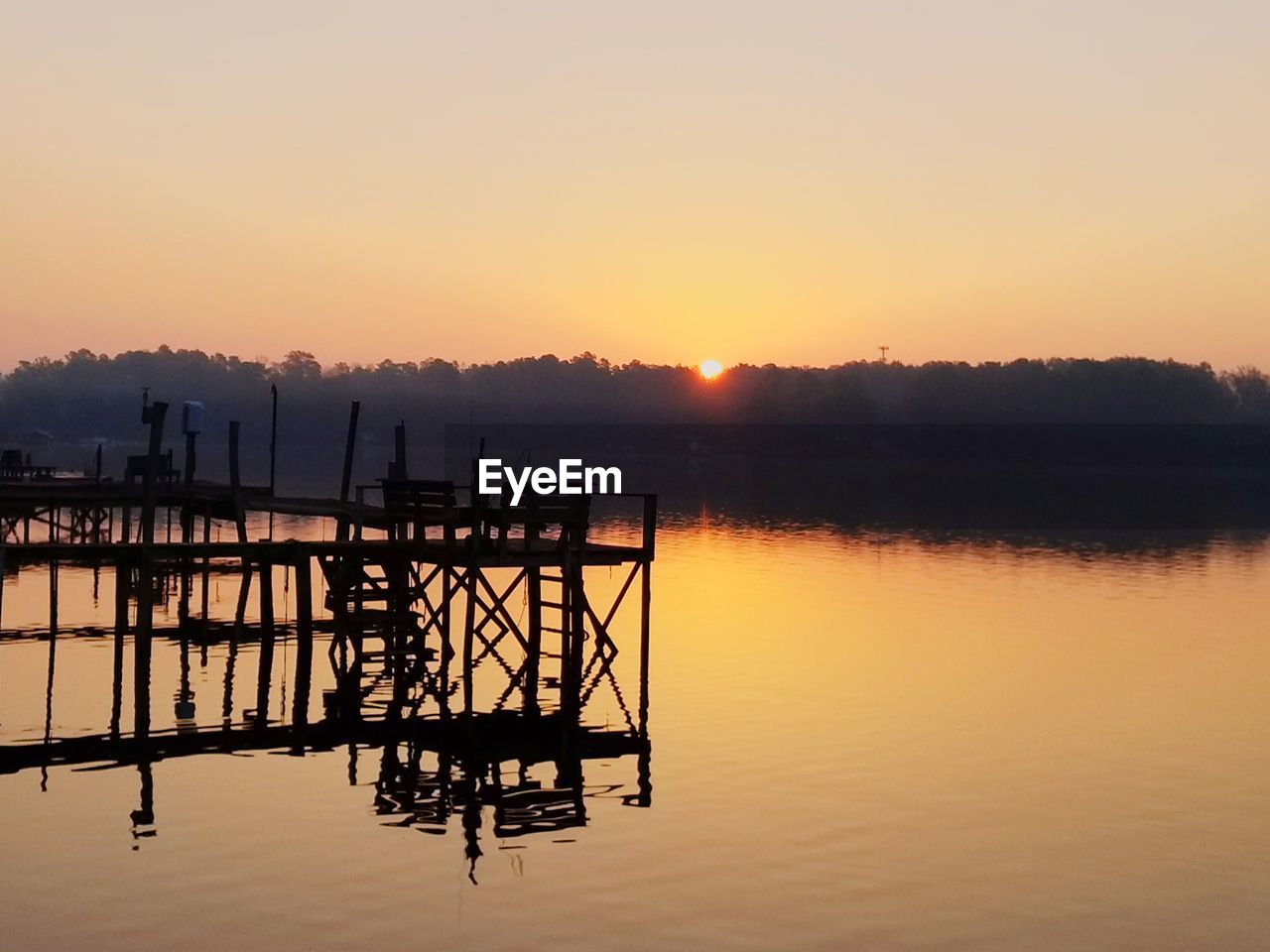 Silhouette pier on lake against sky during sunrise