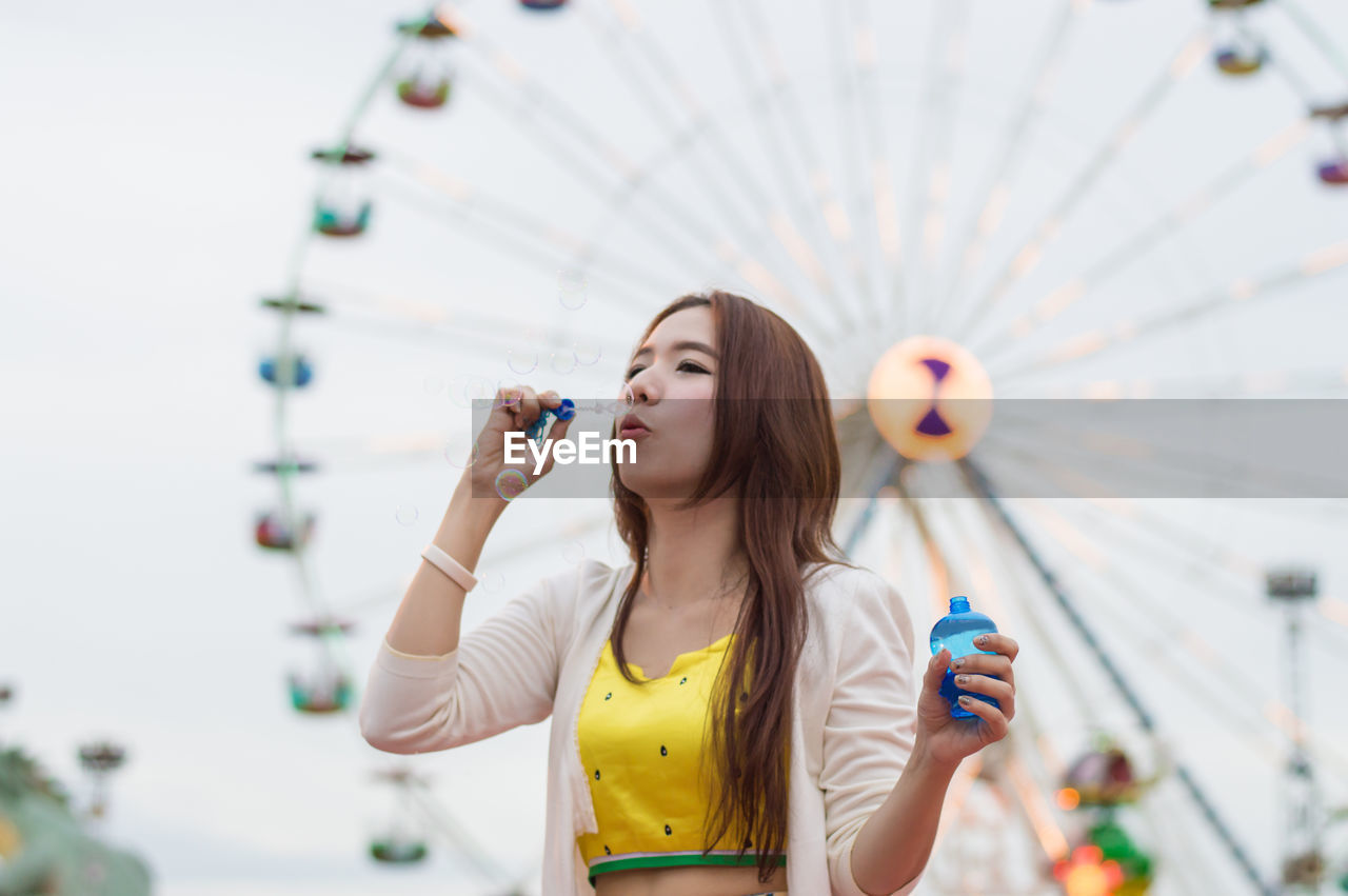 Young woman blowing bubbles while standing in amusement park