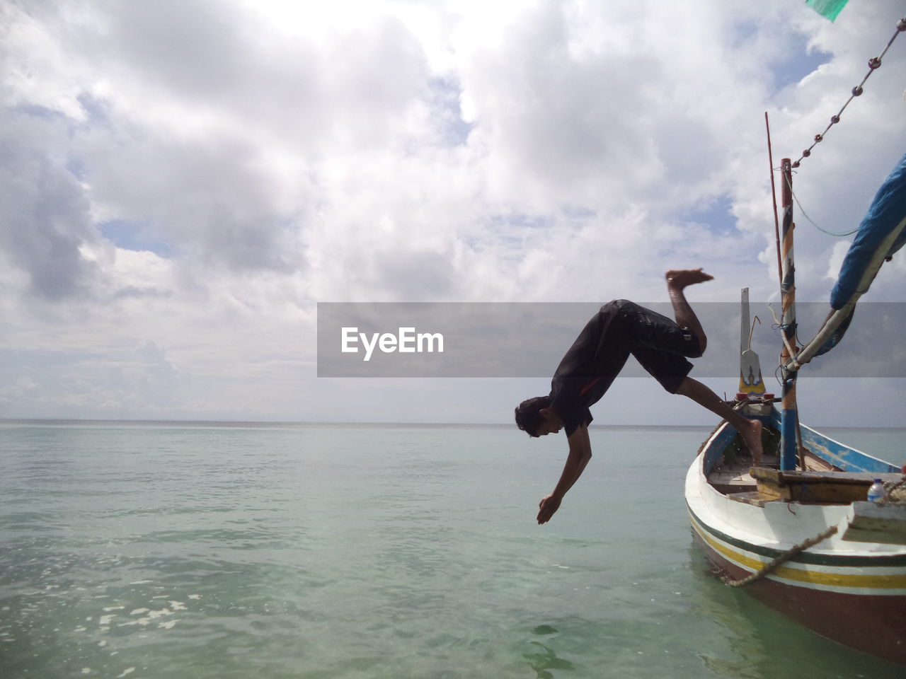 Man diving into sea against cloudy sky