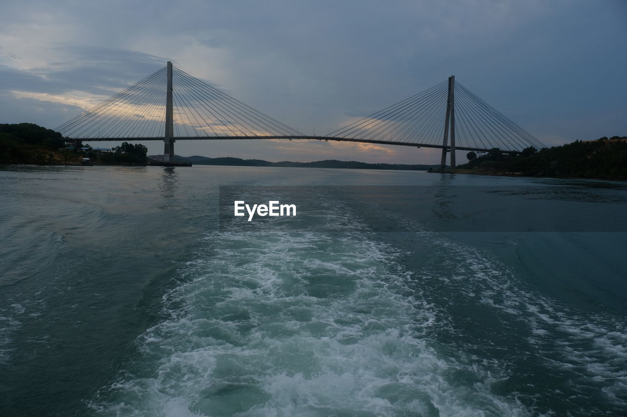 water, bridge, architecture, built structure, sky, suspension bridge, sea, transportation, travel destinations, nature, tourism, travel, scenics - nature, beauty in nature, cloud, engineering, city, motion, surfing, bay, environment, bay of water, wave, landscape, water sports, dramatic sky, outdoors, land, beach, tranquility, tranquil scene, cityscape, long exposure, building exterior, urban skyline, reflection, waterfront, sports, horizon, dusk, day, splashing, idyllic, cable-stayed bridge, blue, shore, holiday, sunset, coastline, fog, atmospheric mood