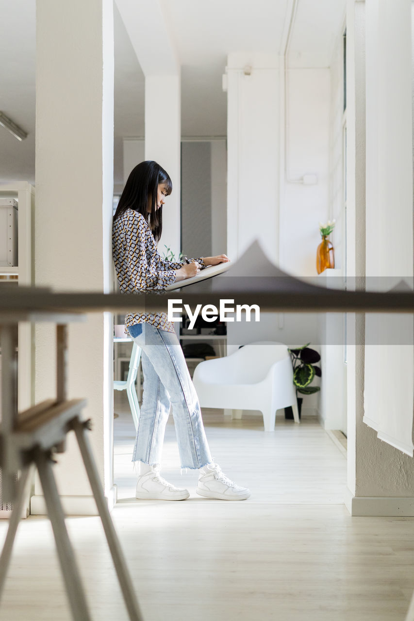 Businesswoman writing while leaning on column at office