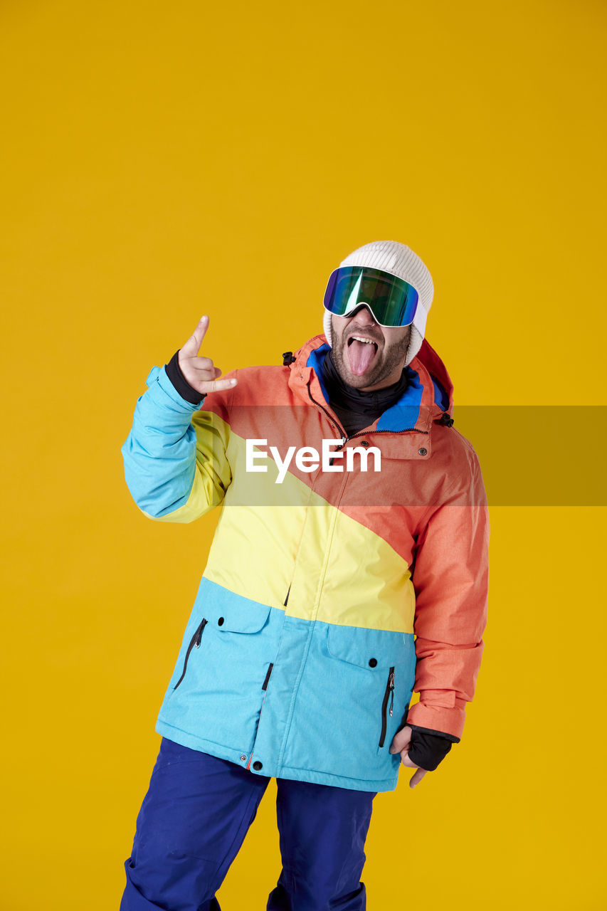 yellow, colored background, one person, studio shot, adult, yellow background, hood, clothing, men, portrait, sports, emotion, young adult, standing, indoors, fun, happiness, three quarter length, person, vibrant color, looking at camera, helmet, fashion, smiling, sports clothing, lifestyles, copy space, sunglasses, outerwear, sports equipment, vitality