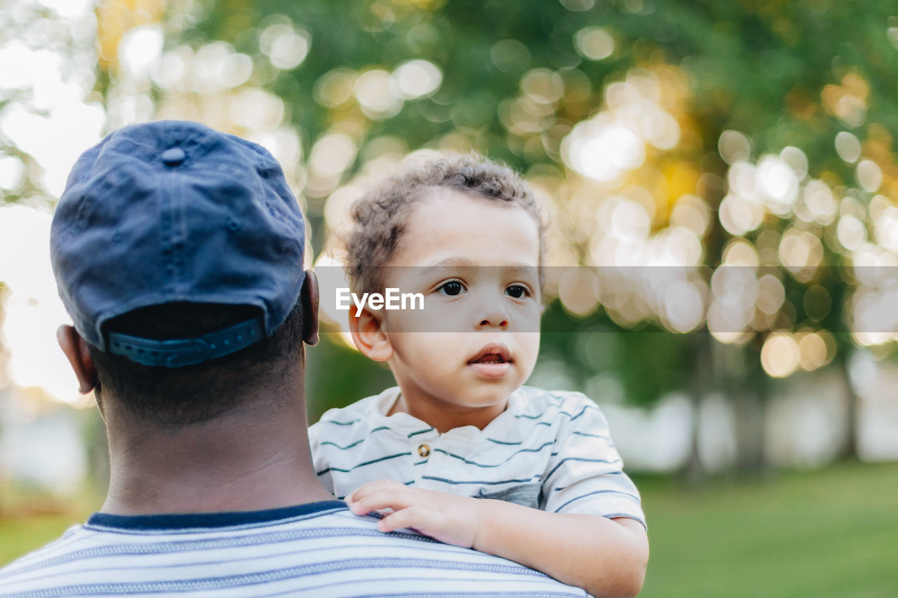 Young millennial african american father and mixed race diverse son bonding at park summer day