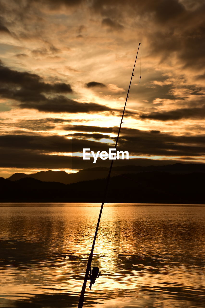 Silhouette fishing rod on sea against sky during sunset