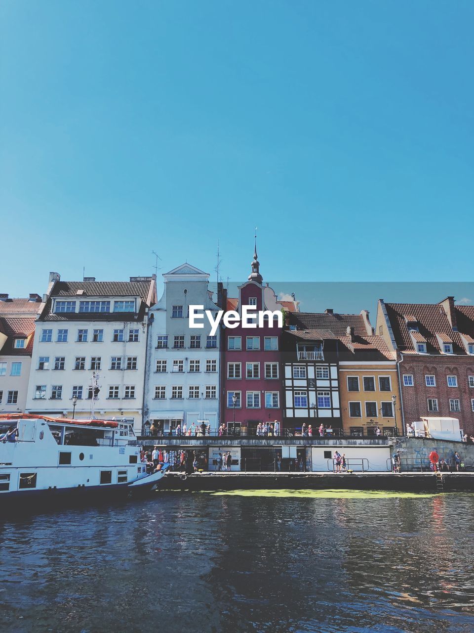 Buildings by river against clear blue sky