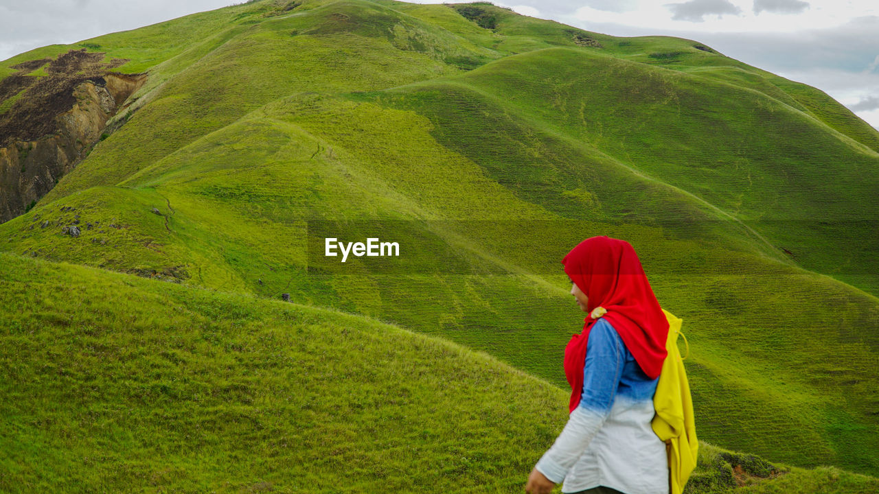 Woman walking on green hill against sky
