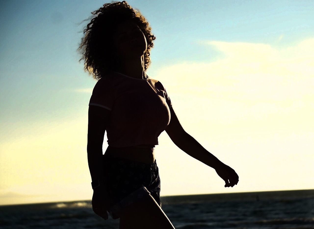 Woman walking by sea against sky during sunset