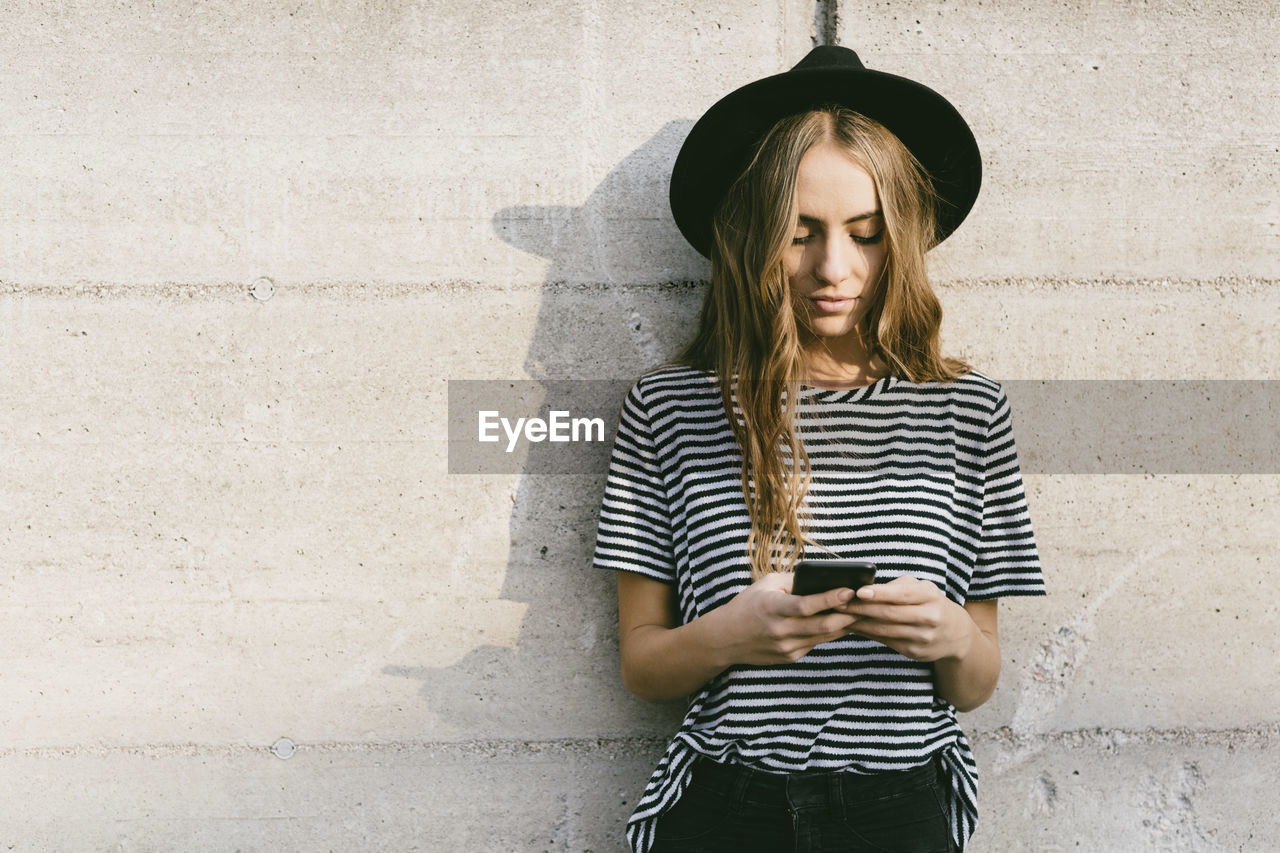 Portrait of fashionable young woman wearing hat using smartphone