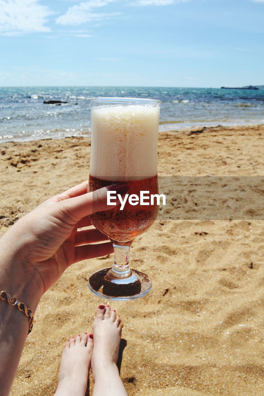 Close-up of woman holding beer glass against beach