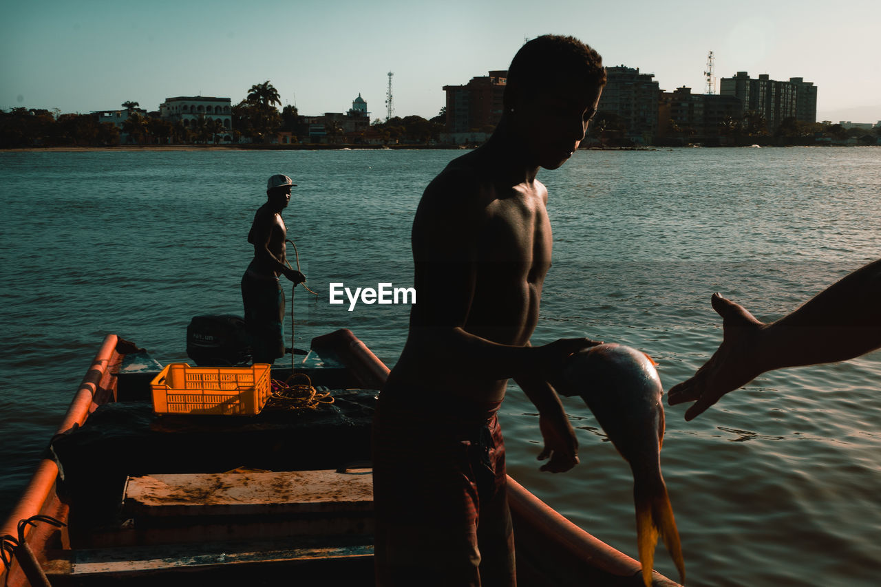 MEN SITTING ON SHORE AGAINST SEA