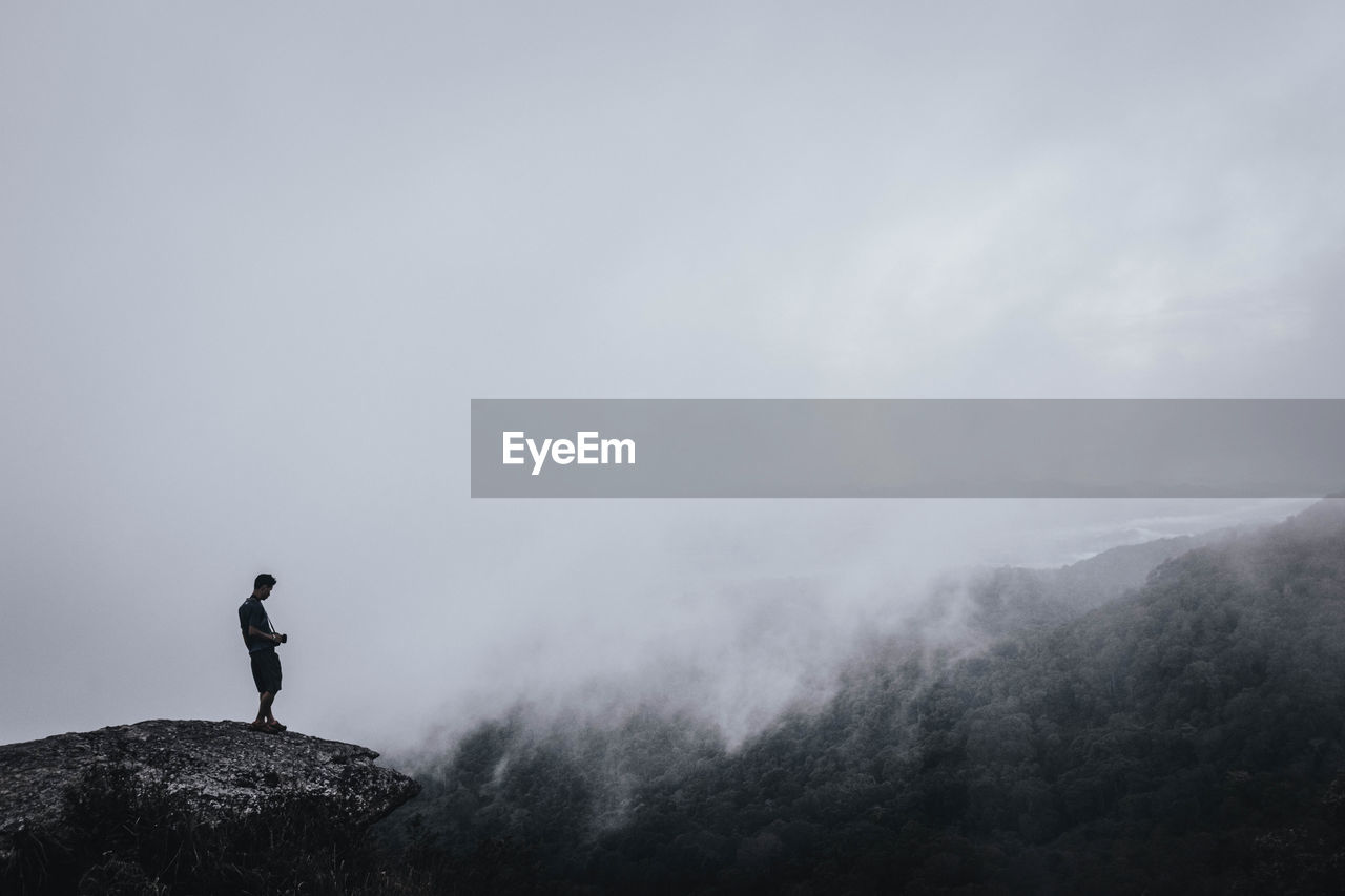 Side view of man standing on mountain against cloudy sky