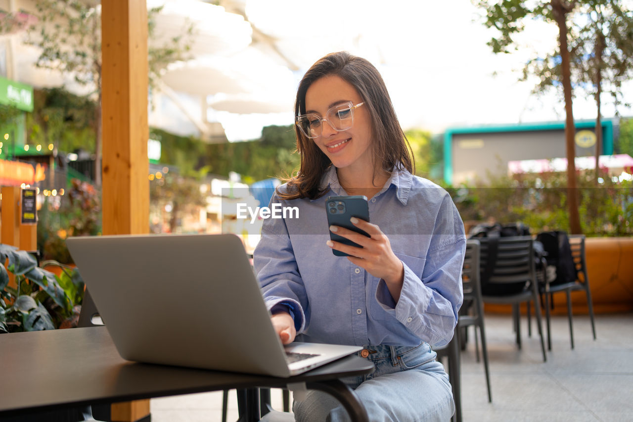 young woman using mobile phone while sitting on table in cafe