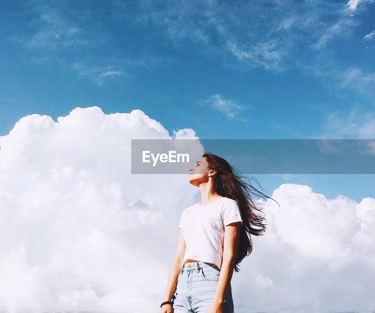 Low angle view of young woman standing against cloudy sky