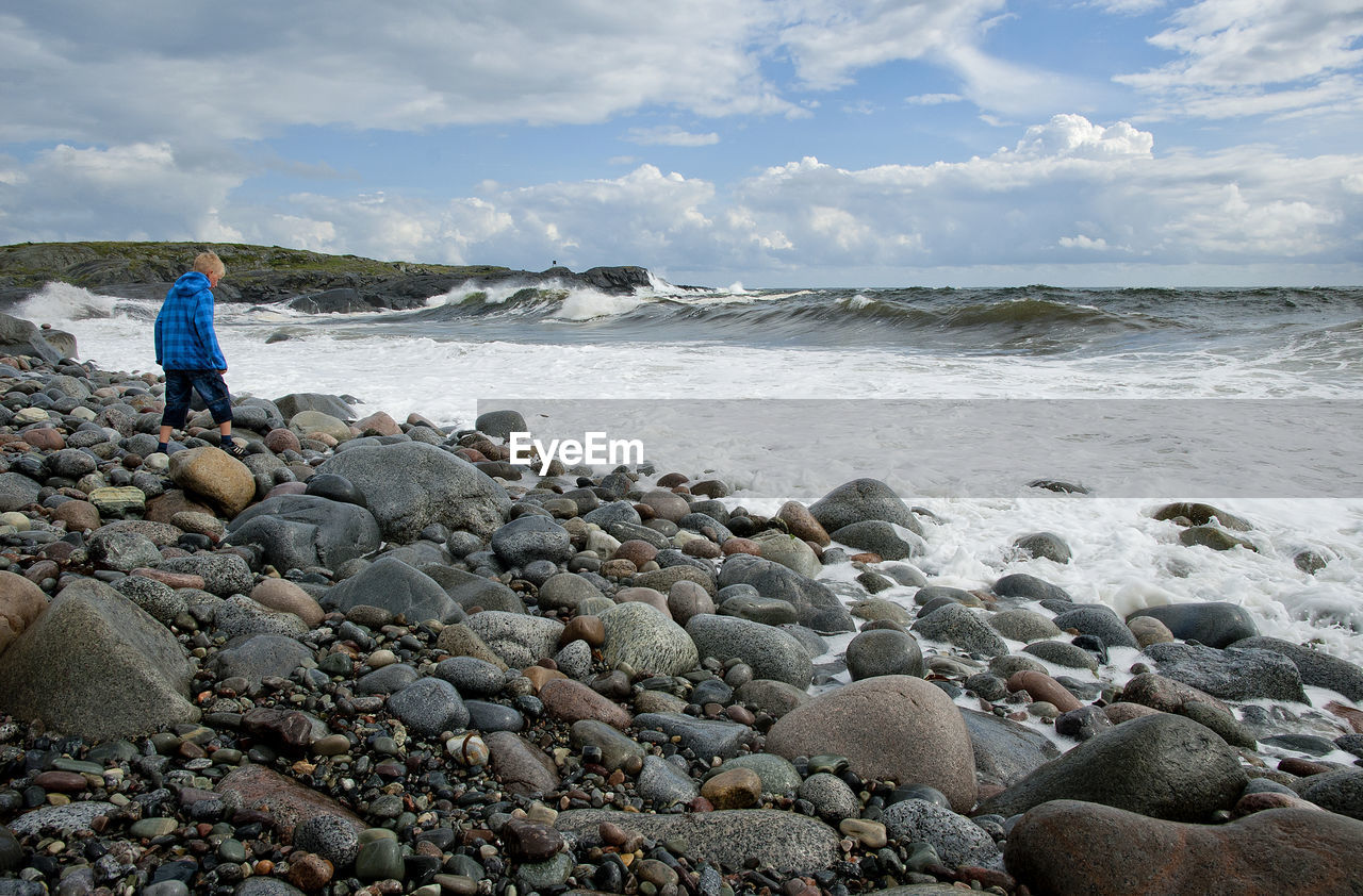 Man standing on rocks at beach against sky