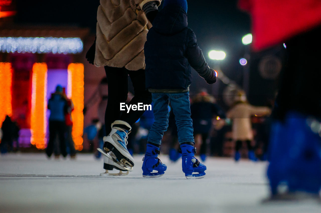 Low section of person with child ice skating on rink at night