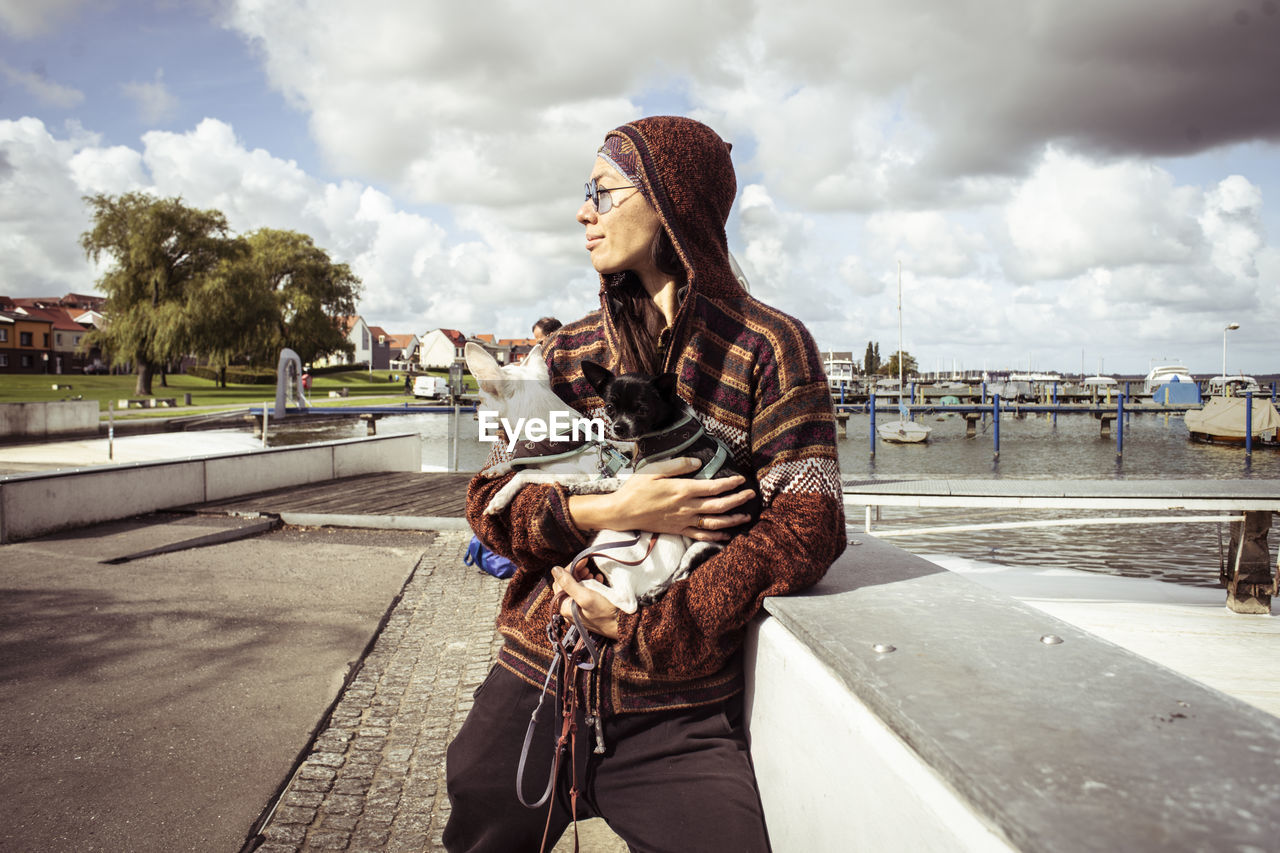 Strong asian woman stands at water dock with two small dogs in sun