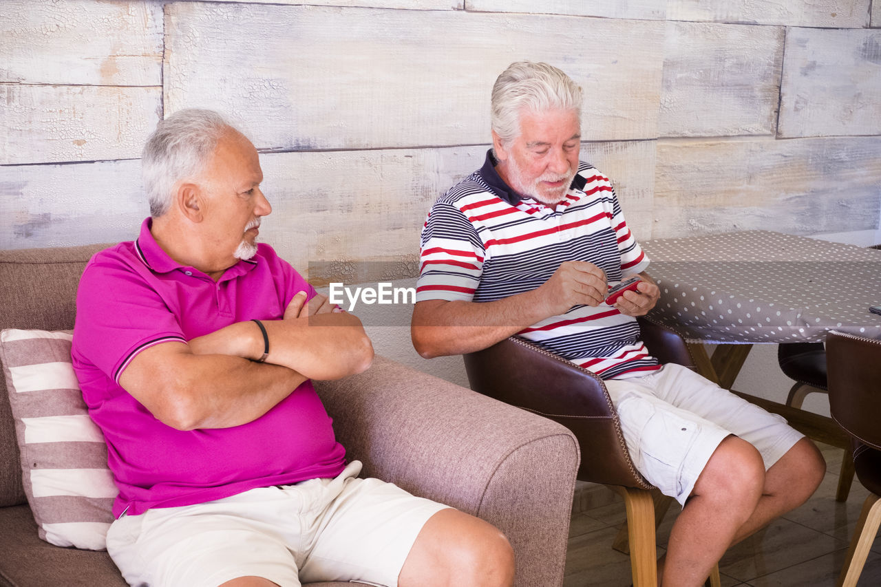 Senior friends sitting against wall at home