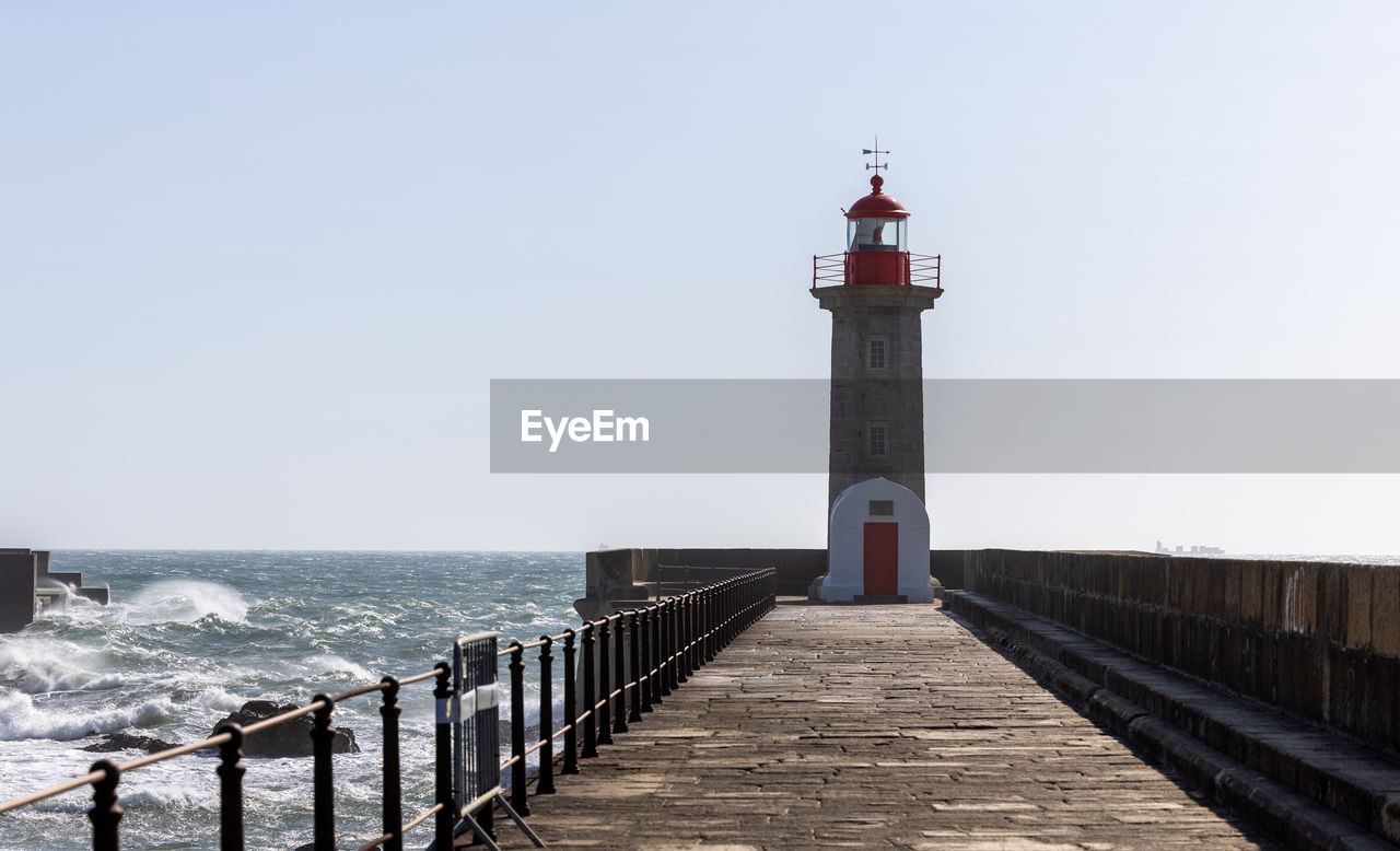 lighthouse, sea, architecture, water, guidance, built structure, sky, tower, security, coast, beach, building exterior, protection, walkway, nature, building, horizon over water, clear sky, horizon, ocean, boardwalk, pier, railing, breakwater, travel destinations, land, day, no people, scenics - nature, coastline, the way forward, travel, outdoors, beauty in nature, tranquility, sunlight, shore, sunny, tourism, history, tranquil scene, wood, jetty, footpath, the past, non-urban scene, copy space, environment