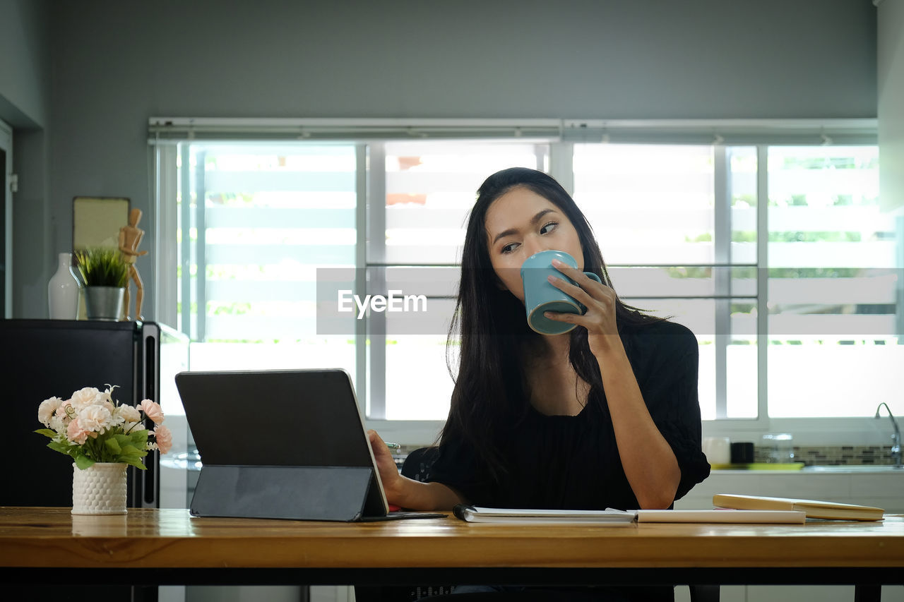 Businesswoman drinking coffee while looking at laptop