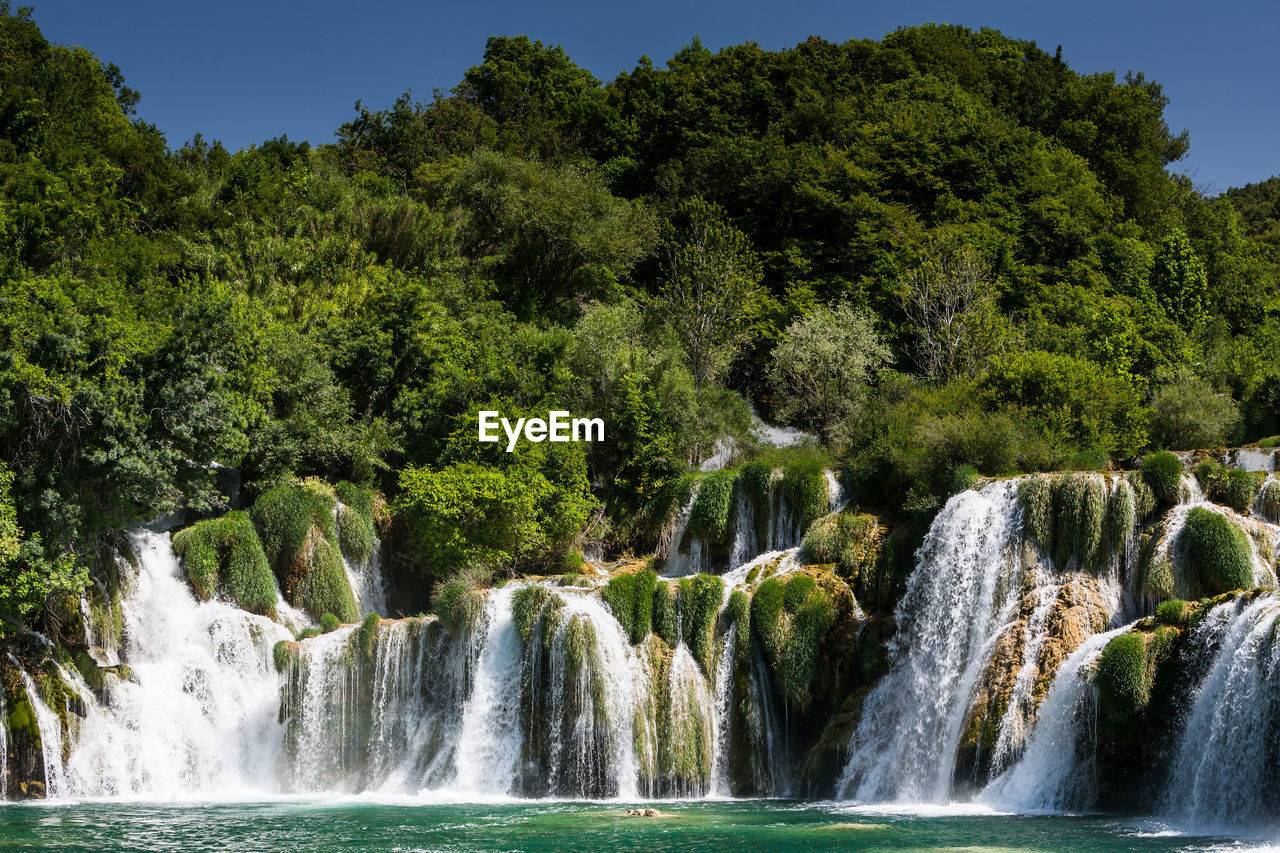 Scenic view of waterfall in forest against clear sky