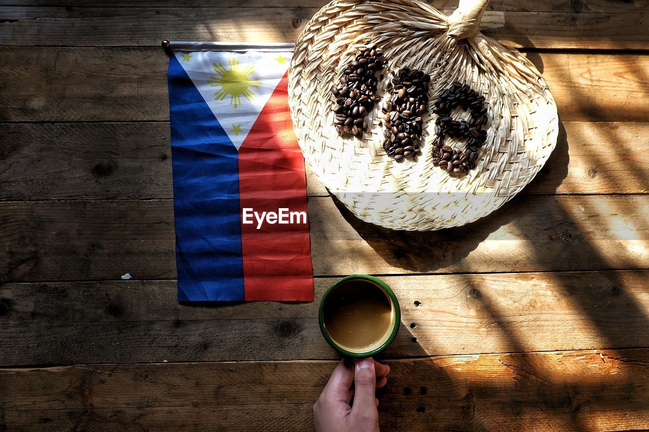 Cropped hand holding coffee in front of philippines flag and number on table