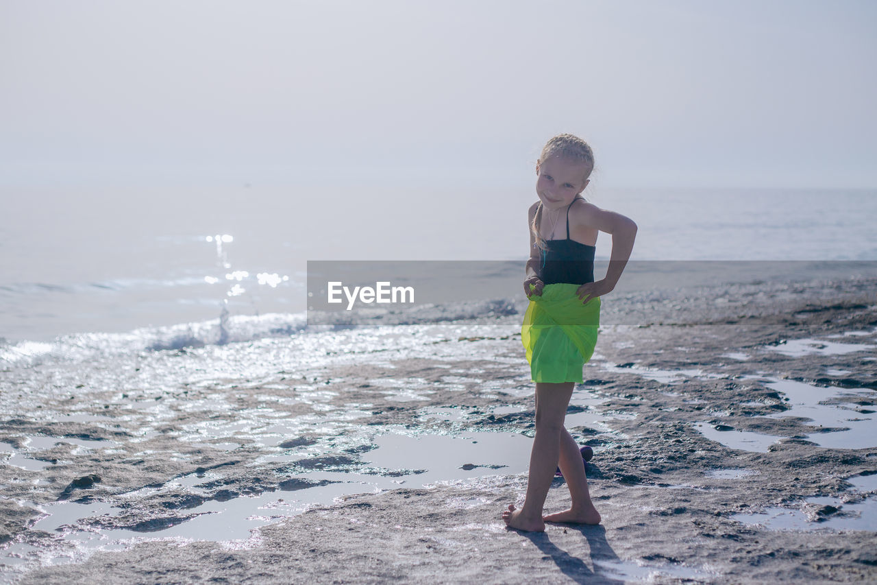 Portrait of cute girl standing at beach against sky