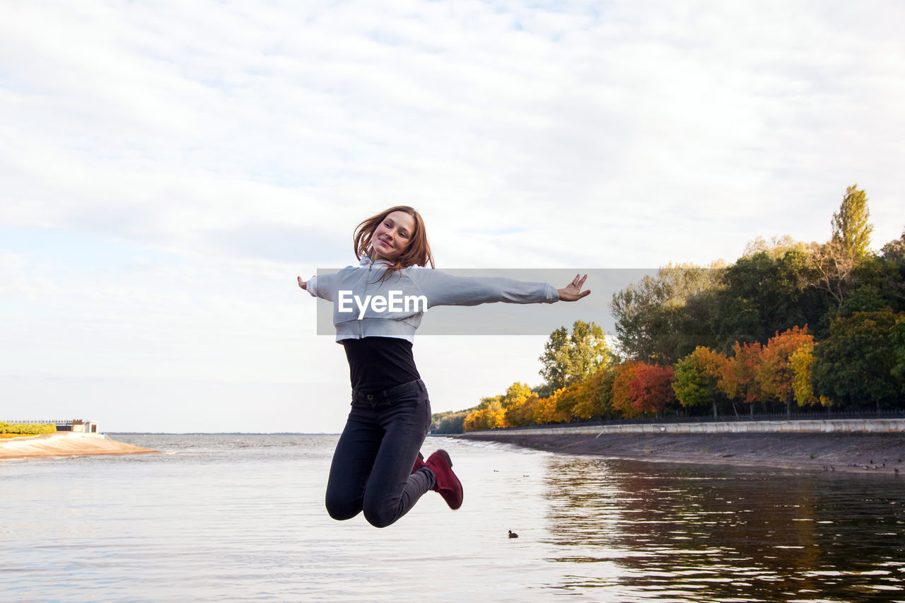 Full length of man jumping in lake against sky