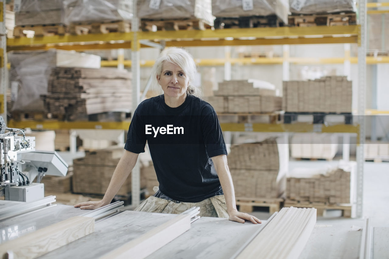 Portrait of mature female worker standing by wooden planks at table in industry