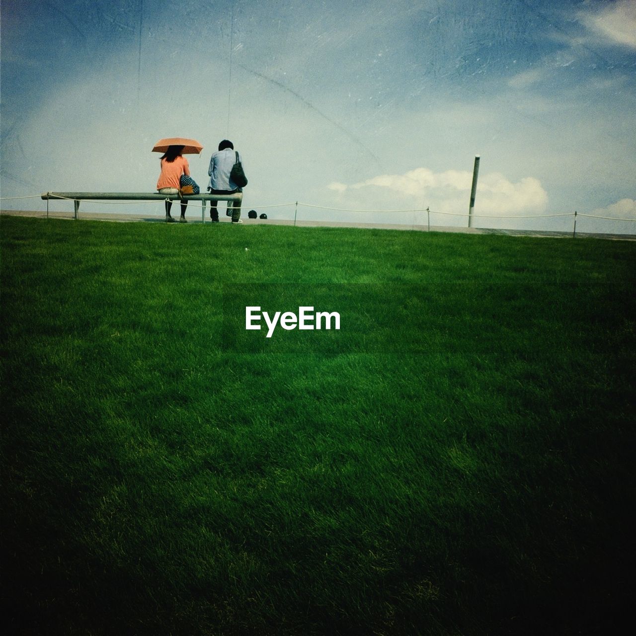 PEOPLE WALKING ON GRASSY FIELD AGAINST SKY