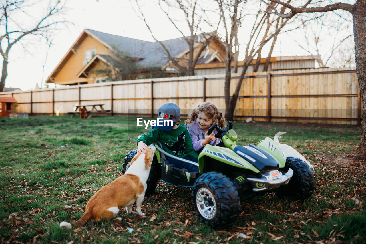 Young brother and sister sitting in battery powered car petting corgi