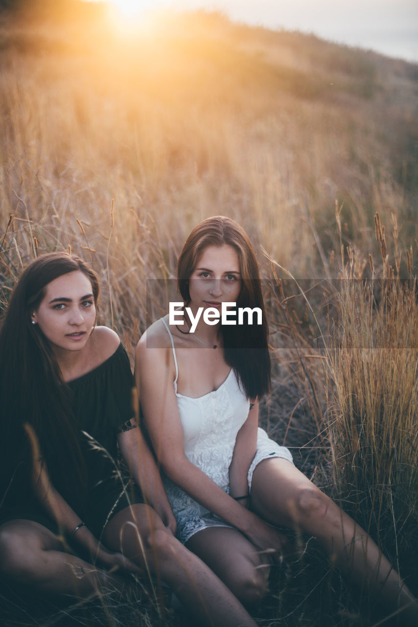 Female friends sitting on land against sky during sunset