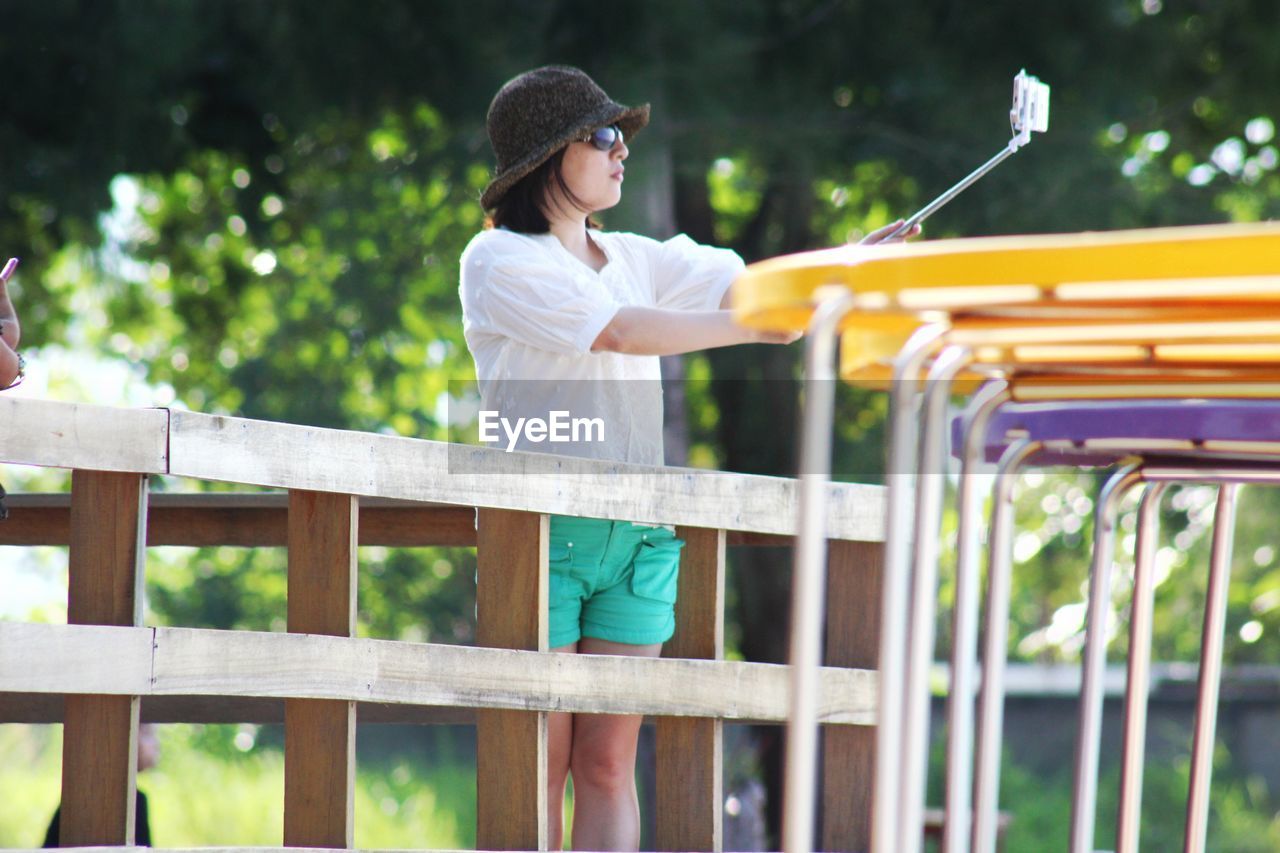 Woman taking selfie though smart phone while standing by fence