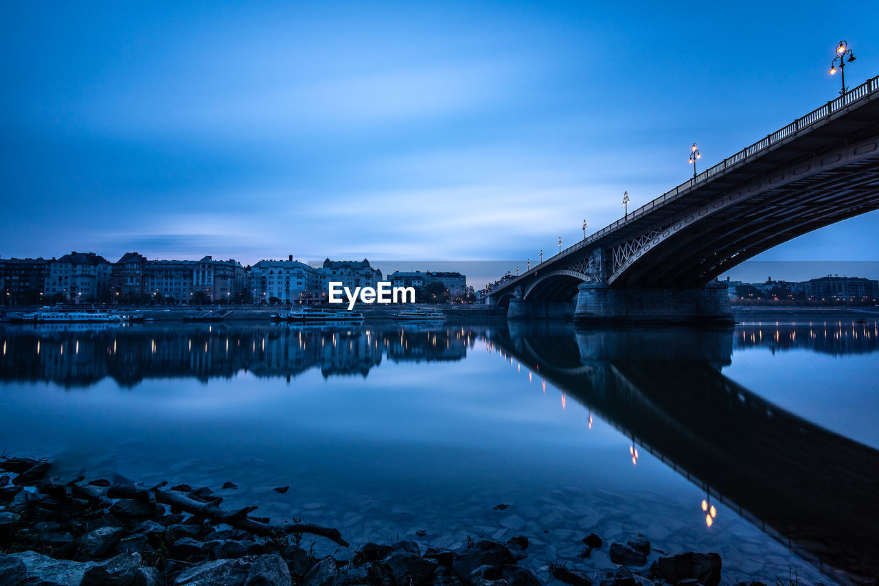 Bridge over river in city against blue sky at dusk