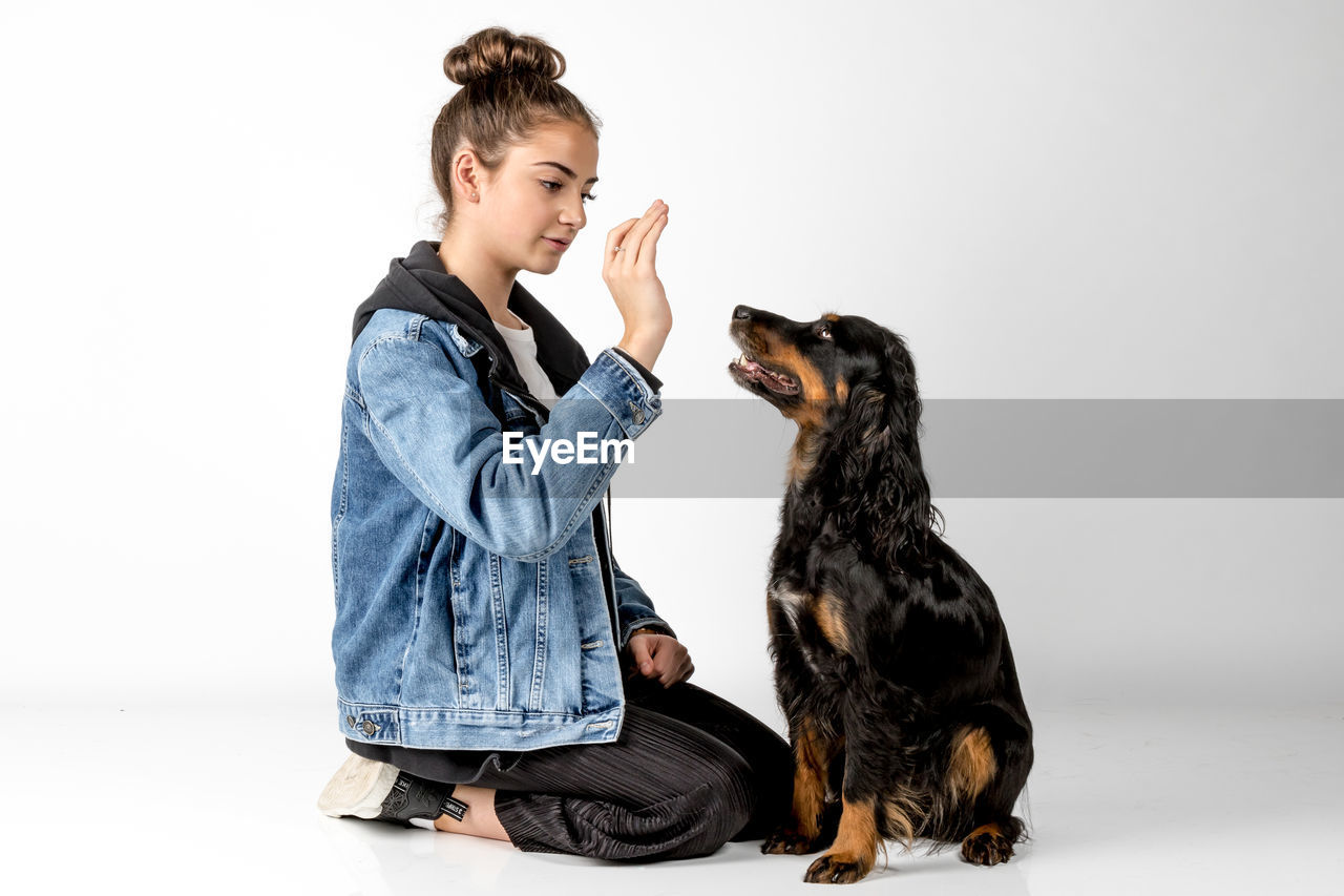 Full length of young woman playing with puppy against white background