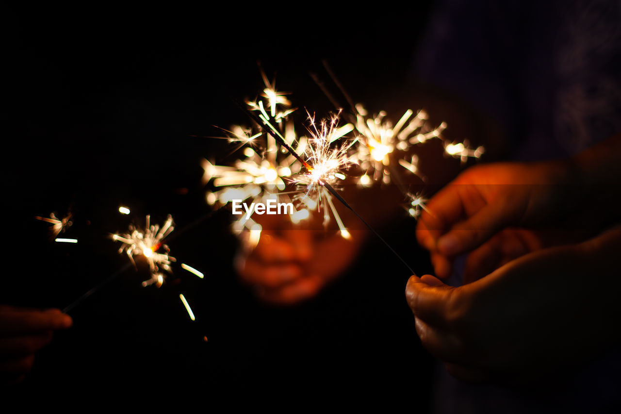 Cropped image of people holding sparklers against black background