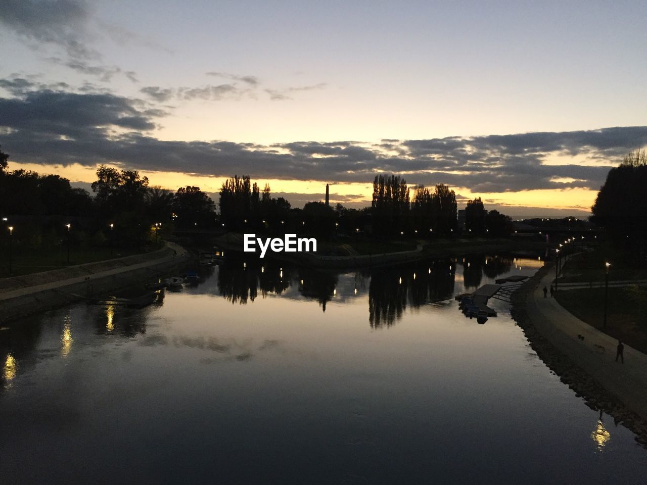 REFLECTION OF SILHOUETTE TREES IN WATER AGAINST SKY