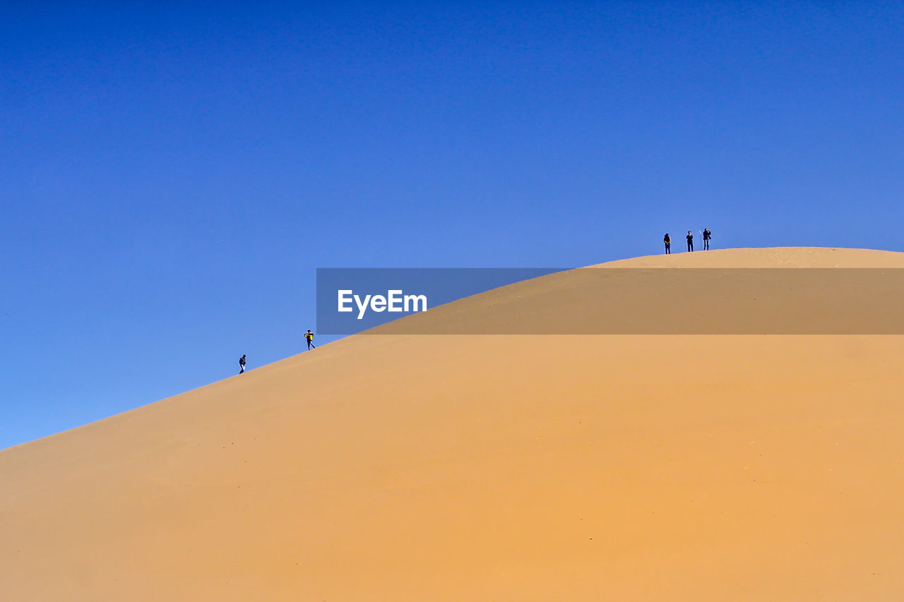 People on sand dune against clear sky