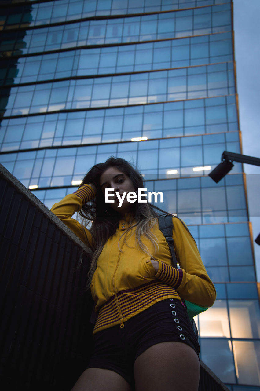 Low angle portrait of young woman standing against building