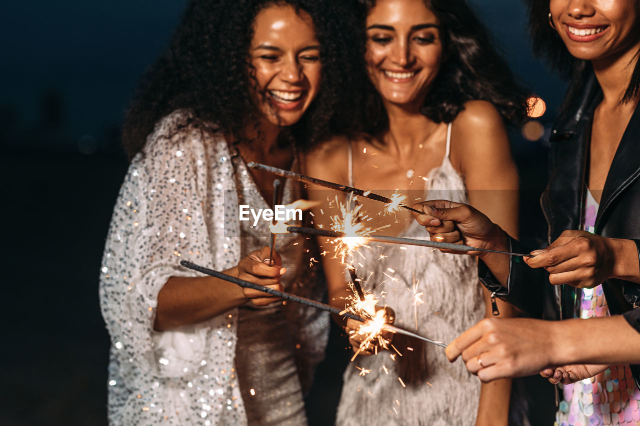 Cheerful female friends holding sparklers at night